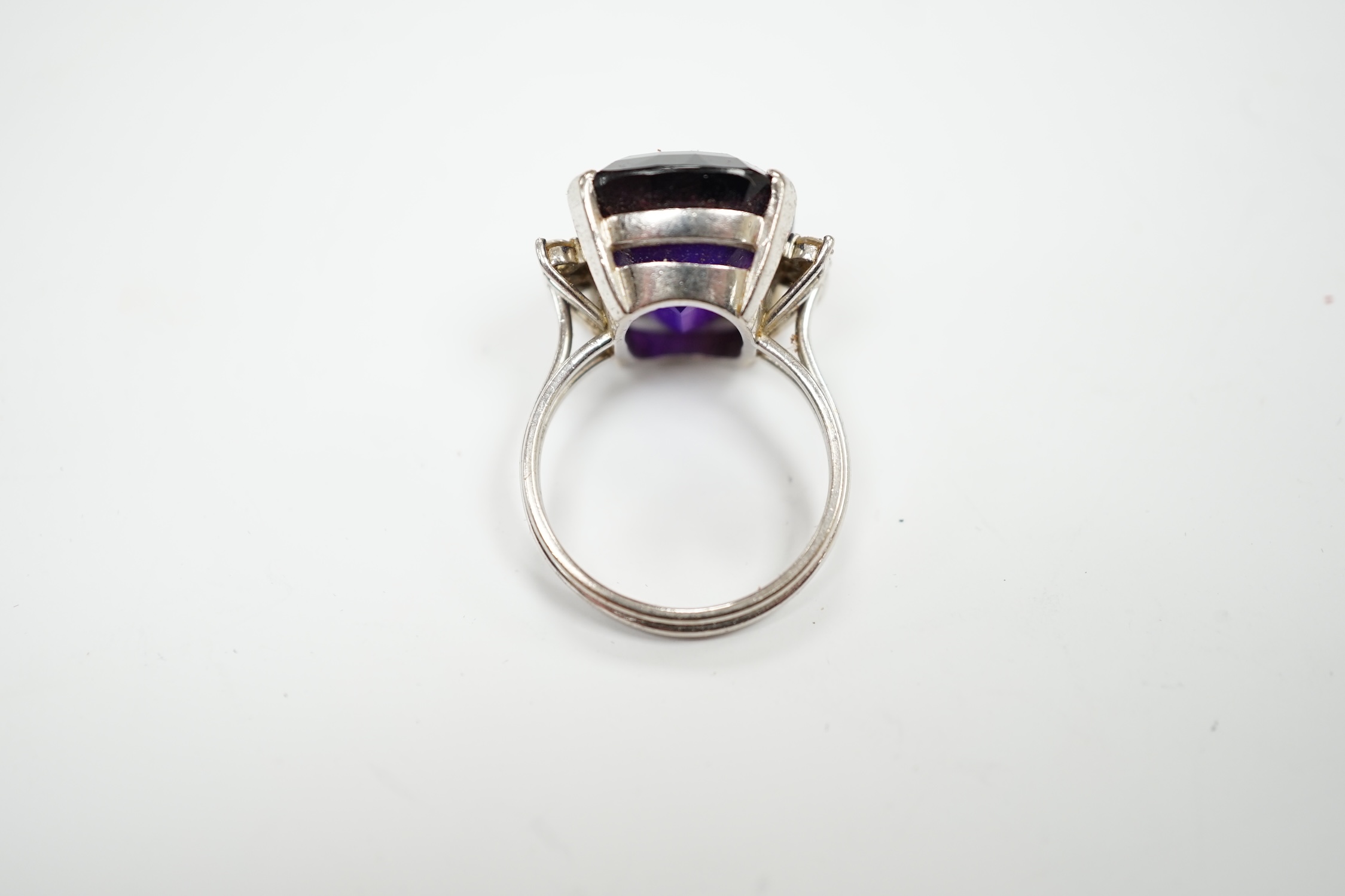 A white metal and single stone cushion cut amethyst set dress ring, with six stone diamond set shoulders, size O, gross weight 9.2 grams.